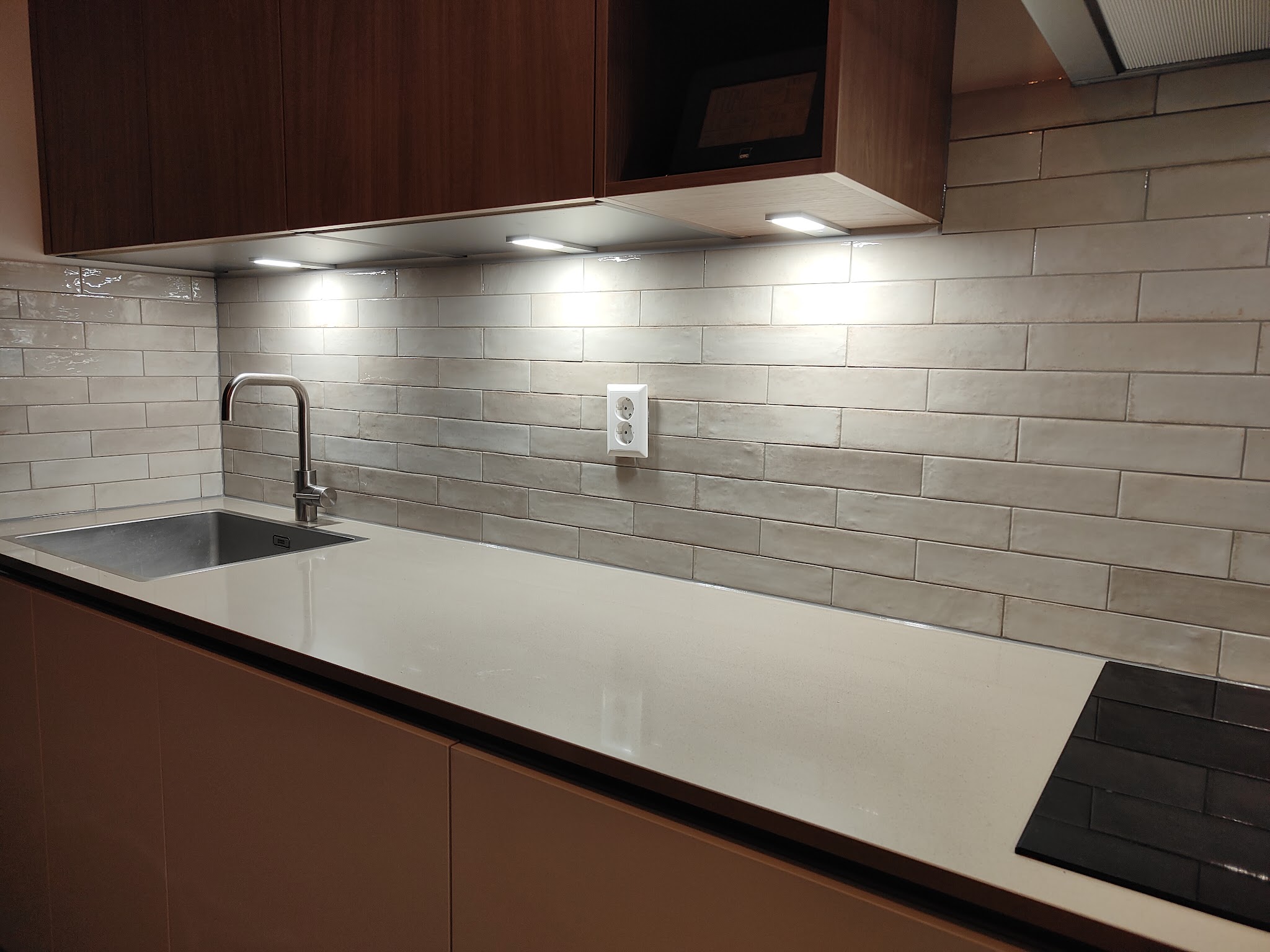 Keukenwand met lange glanzende witte tegels achter een licht werkblad